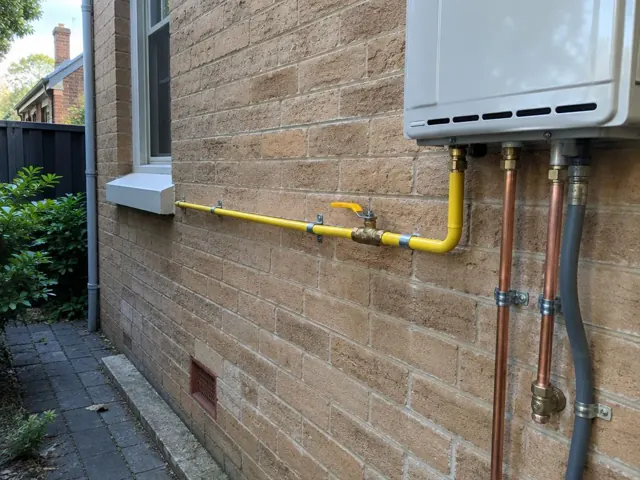 External gas piping and wall-mounted appliance on a brick house wall with window and side path in North Sydney
