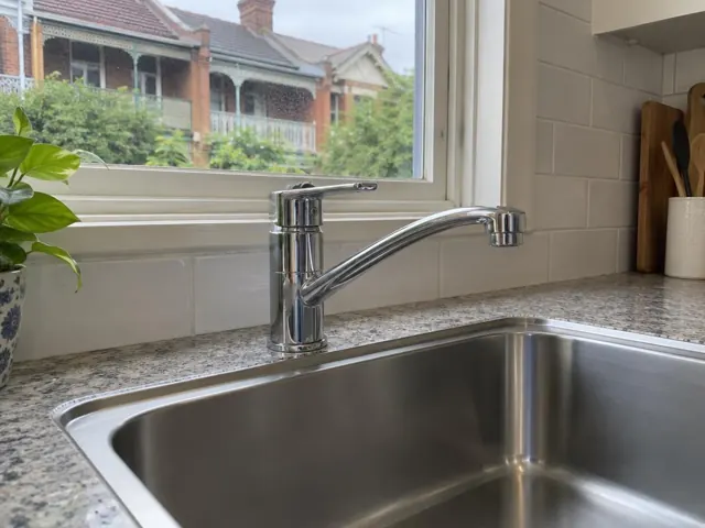 Chrome kitchen mixer tap above stainless sink and speckled bench by a window in North Sydney